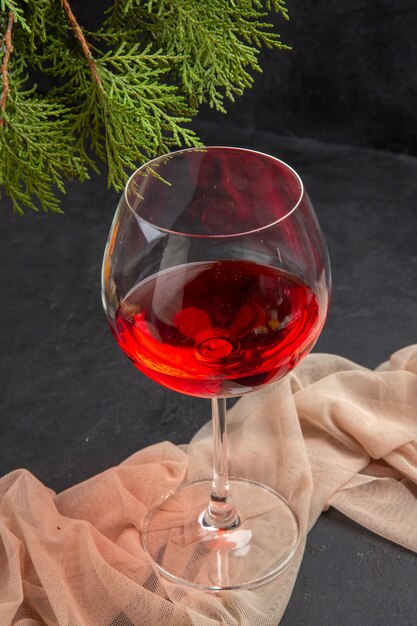 Oben Blick auf köstlichen Rotwein in einem Glasbecher auf Handtuch und Tannenzweigen auf dunklem Hintergrund