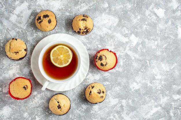Oben Blick auf leckere kleine Cupcakes mit Schokolade um eine Tasse schwarzen Tee auf der rechten Seite auf Eisfläche