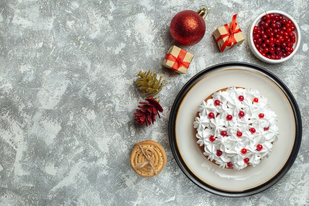 Oben Blick auf leckeren Kuchen mit Sahne-Johannisbeere auf einem Teller und Geschenkboxen gestapelte Kekse Koniferenkegel auf der linken Seite auf grauem Hintergrund