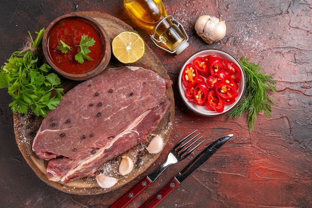 Oben Blick auf rotes Fleisch auf Holztablett und Knoblauch grüner Ketchup und gehackte Pfefferölflasche auf dunklem Hintergrund