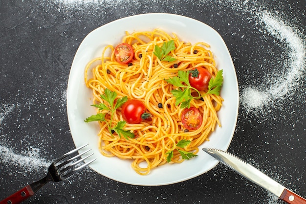 Oben Blick auf vegane Spagetti mit Tomaten und Grün auf einem quadratischen Tellerbesteck auf schwarz-weißem Hintergrund