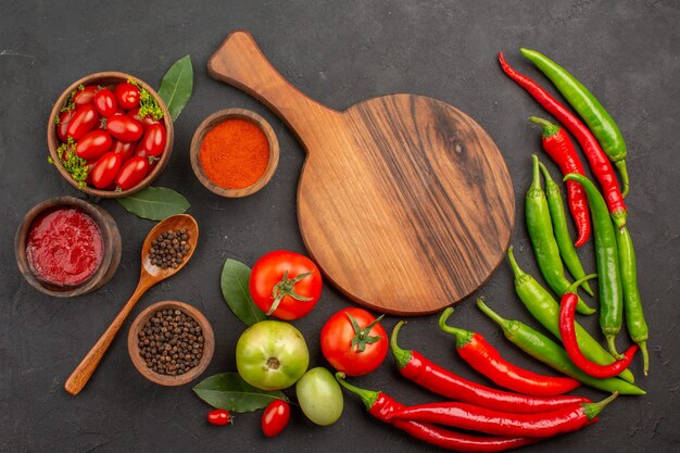 Oben entfernte Ansicht eine Schüssel Kirschtomaten scharfe rote und grüne Paprikaschoten und Tomaten Lorbeerblätter Schalen mit Ketchup-Paprika-Pulver und schwarzem Pfeffer und ein Schneidebrett auf dem Boden