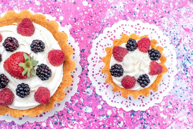 Oben nähere Ansicht von kleinen cremigen Kuchen mit verschiedenen Beeren auf hellem Weiß