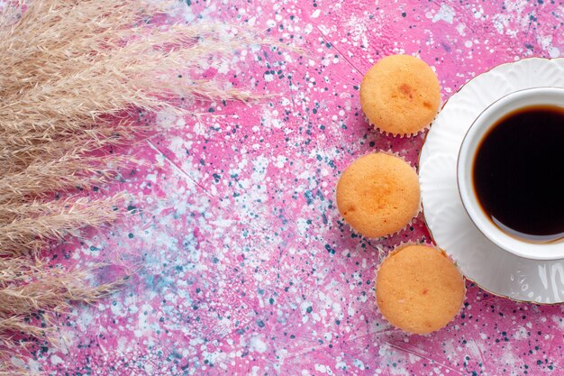 Oben Nahansicht der Tasse Tee mit kleinen Kuchen auf rosa Oberfläche