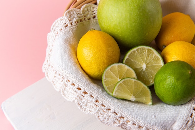 Oben Nahansicht des Korbes mit Zitrusfrüchten Zitronen und Limetten innen auf rosa Oberfläche