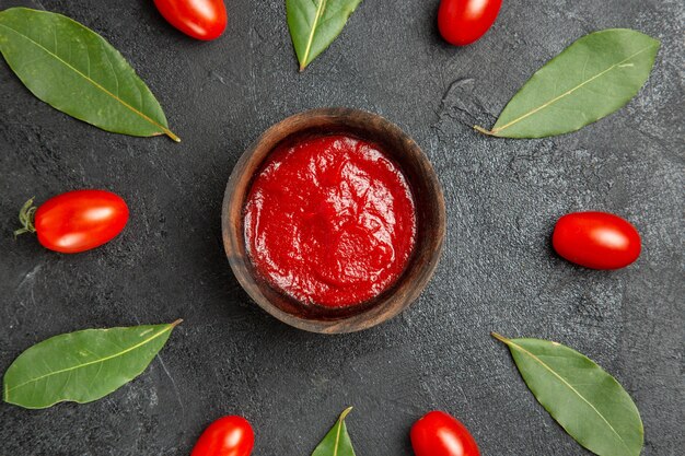 Oben Nahansicht eine Schüssel Ketchup um Kirschtomaten und Lorbeerblätter auf dunklem Boden