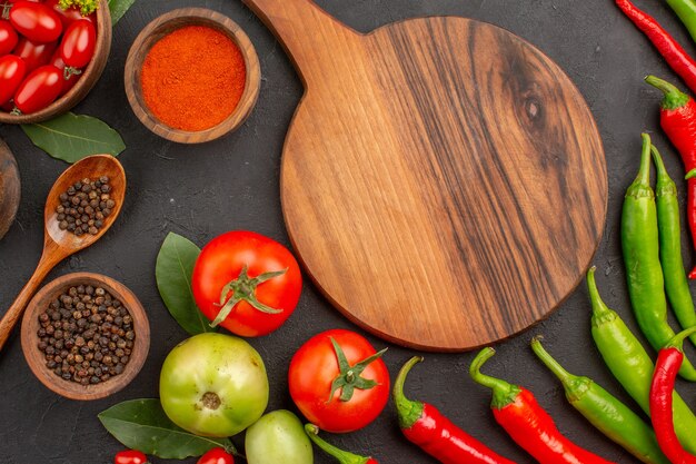 Oben Nahansicht eine Schüssel Kirschtomaten scharfe rote und grüne Paprika und Tomaten Lorbeerblätter Schalen mit Ketchup-Paprika-Pulver und schwarzem Pfeffer und ein Schneidebrett auf dem Boden