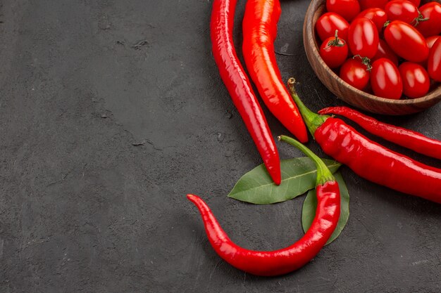 Oben Nahansicht Halbkreis von roten Peperoni und Lorbeerblättern und einer Schüssel Kirschtomaten auf der rechten Seite des schwarzen Tisches