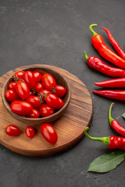 Kostenloses Foto oben nahansicht rote paprika und pay-blätter und eine schüssel kirschtomaten auf dem schneidebrett auf schwarzem tisch mit freiem platz