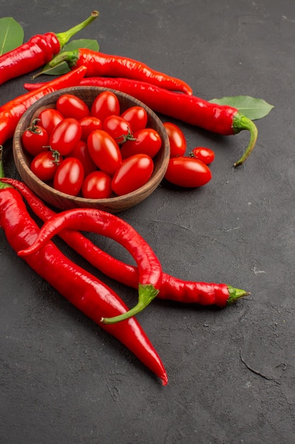 Oben Nahansicht scharfe rote Paprika und Lorbeerblätter und eine Schüssel Kirschtomaten auf dem schwarzen Tisch