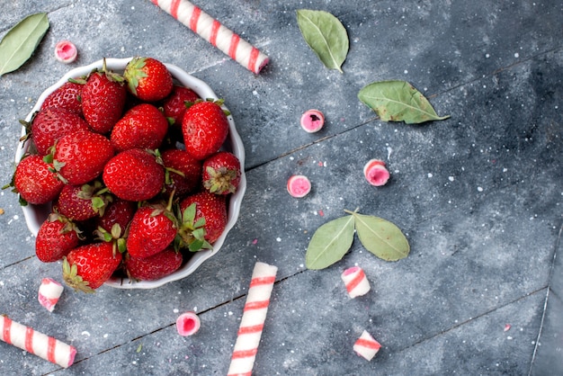 Kostenloses Foto oben nahansicht von frischen roten erdbeeren innerhalb platte zusammen mit stock bonbons auf grau, fruchtbeere frische süßigkeiten süß