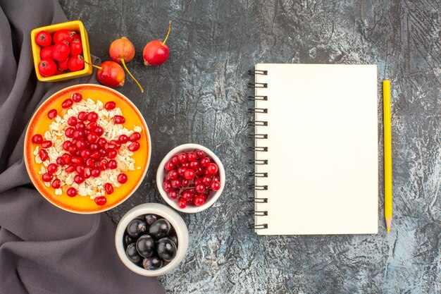 Oben Nahaufnahme Ansicht Beeren Haferflocken mit Granatäpfeln bunten Beeren auf dem Tischtuch Notizbuch