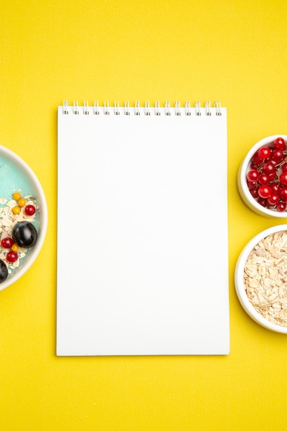 Oben Nahaufnahme Ansicht Beeren Schalen der bunten Beeren Haferflocken weißes Notizbuch