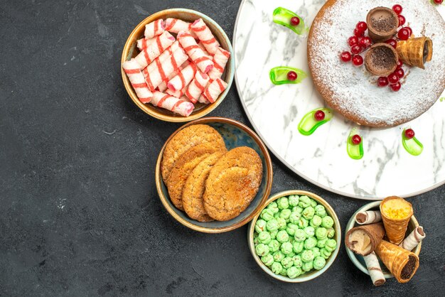 Oben Nahaufnahme Ansicht ein Kuchen ein Kuchen mit Beeren Waffeln Schalen von bunten Süßigkeiten Kekse