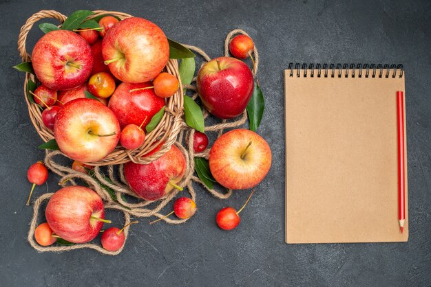 Oben Nahaufnahme Ansicht Obstkorb mit Äpfeln Kirschen neben den Früchten und Seil Notizbuch Bleistift