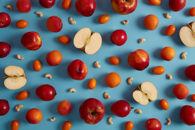 Oben Schuss von roten reifen Äpfeln, Pfirsichen, Tomarillo, Cumquat und nährstoffhaltigen Cashewnüssen auf blauem Hintergrund. Kreative Komposition köstlicher Früchte. Süßes Essen mit Viamins, gesundes Ernährungskonzept