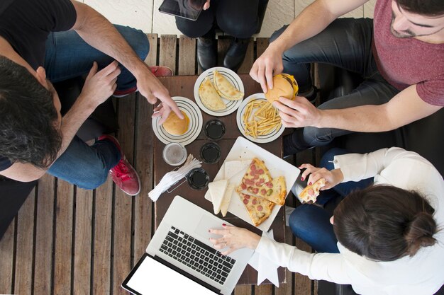 Obenliegende Ansicht der Frau, die Laptop mit seinen Freunden genießen Snack im Restaurant verwendet