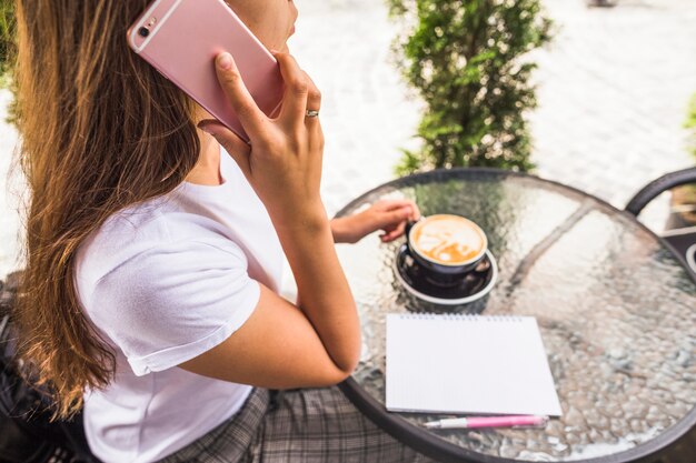 Obenliegende Ansicht der Frau sprechend am Handy, der Tasse Kaffee hält