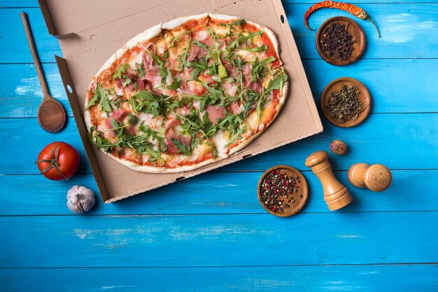 Obenliegende Ansicht der geschmackvollen Pizza mit Bestandteilen auf blauem Holztisch