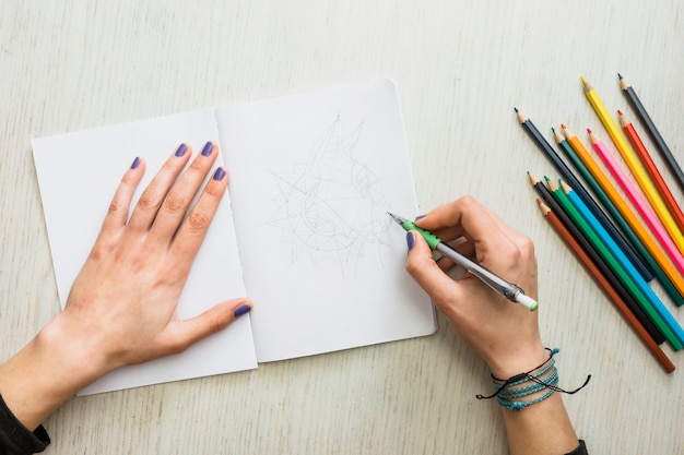 Obenliegende Ansicht der Hand des Menschen, die auf weißem Zeichnungsbuch skizziert