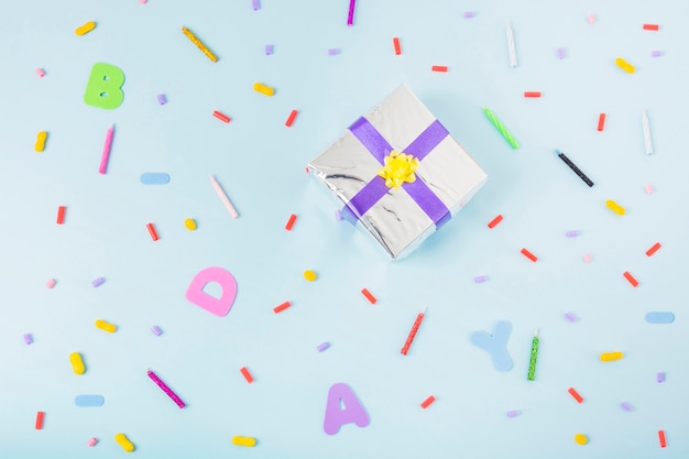 Obenliegende Ansicht der silbernen Geschenkbox umgeben mit Süßigkeiten und Kerzen auf Geburtstag