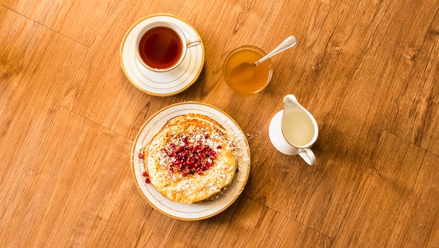 Obenliegende Ansicht des Pfannkuchens mit Honig- und Teeschale auf Holztisch
