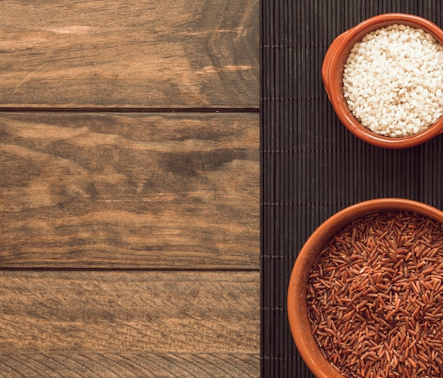 Obenliegende Ansicht des roten Reiskorns des Jasmins und des weißen Reises auf placemat über Holztisch