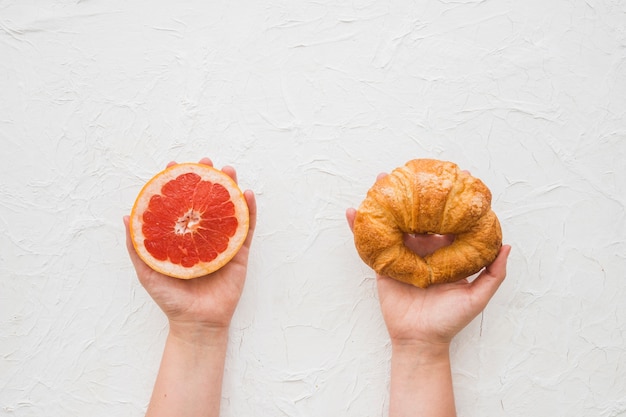 Obenliegende Ansicht von den Händen, die Grapefruitscheibe und -hörnchen über weißem Hintergrund halten