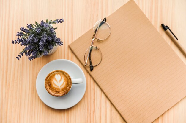 Obenliegende Ansicht von Kaffee Latte, Schreibwaren und Lavendel blühen auf hölzernem Hintergrund