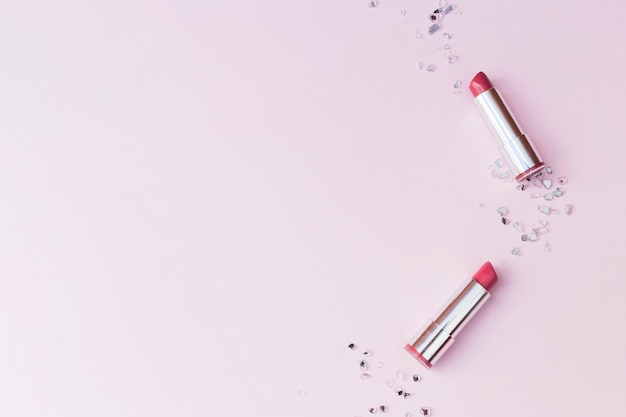 Obenliegende Ansicht von zwei rosa Lippenstiften und von zerquetschten Glasstücken auf rosa Hintergrund