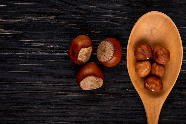 Oberansicht kopieren Raum geschälte Haselnüsse in einem Holzlöffel und in der Schale auf einem schwarzen Holzhintergrund