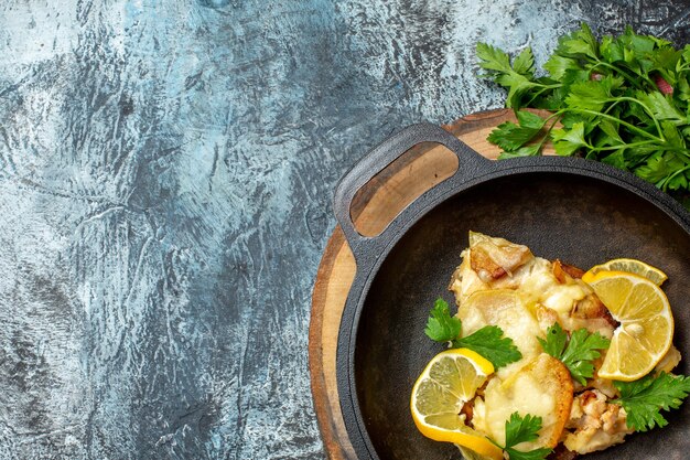 Obere Hälfte Ansicht gebratener Fisch in der Pfanne auf Holzbrettpetersilie auf grauem Tischkopierplatz