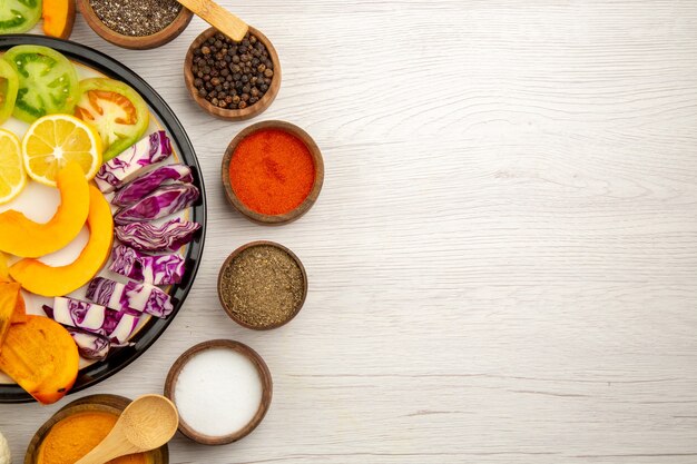 Obere Hälfte Ansicht geschnittenes Gemüse und Obst Kürbis Persimone Rotkohl auf Schwarzplatte verschiedene Gewürze in Schalen Holzlöffel auf Holztisch mit Kopie Platz