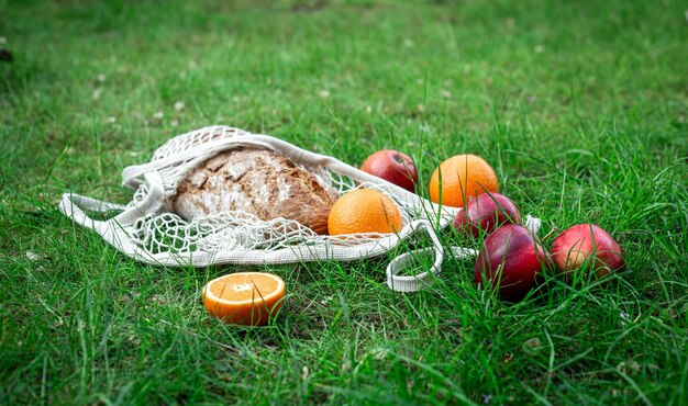 Obst und frisches Brot in einer Schnurtasche im Gras