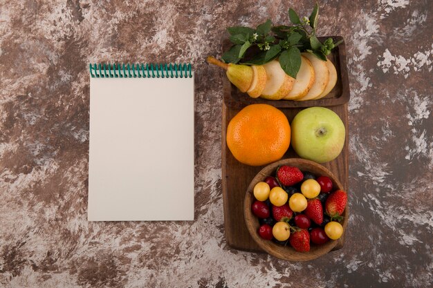 Obstplatte mit Minze auf dem Marmor mit einem Notizbuch beiseite