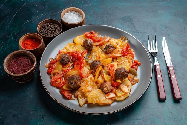 Ofenkartoffeln mit halber Draufsicht mit Fleischbällchen und Gemüse sowie Gewürzen auf dem dunkelblauen Schreibtisch.