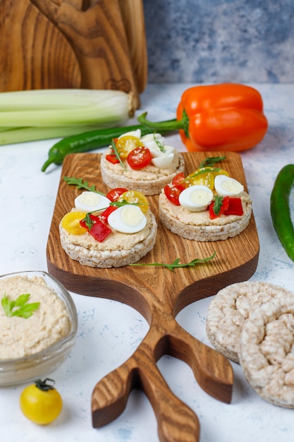 Offene Sandwiches mit Reiskuchen mit Hummus, Gemüse und Wachtelei, gesundes Frühstück oder Mittagessen