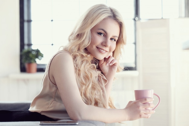 offene schöne blonde Frau mit Tee oder Kaffeetasse