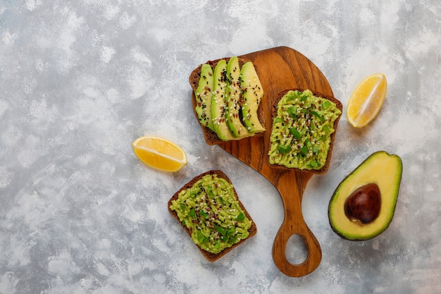 Kostenloses Foto offener toast der avocado mit avocadoscheiben, zitrone, leinsamen, samen des indischen sesams, schwarzbrotscheiben, draufsicht