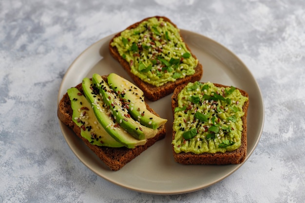 Offener Toast der Avocado mit Avocadoscheiben, Zitrone, Leinsamen, Samen des indischen Sesams, Schwarzbrotscheiben, Draufsicht