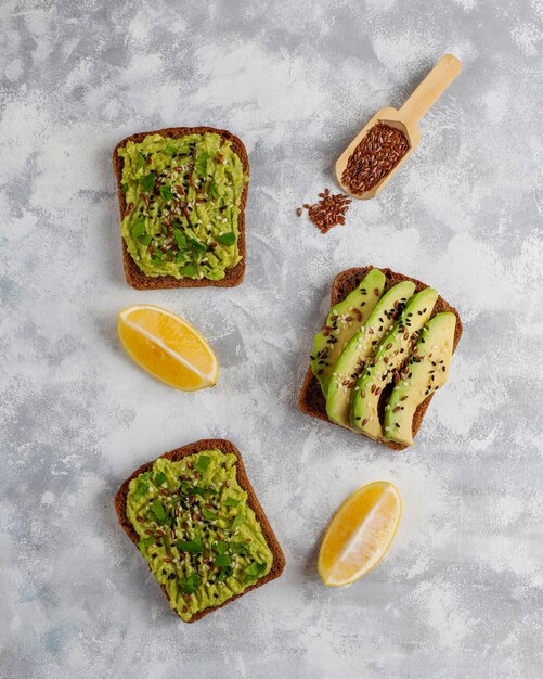 Offener Toast der Avocado mit Avocadoscheiben, Zitrone, Leinsamen, Samen des indischen Sesams, Schwarzbrotscheiben, Draufsicht