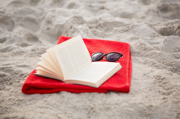 Offenes Buch und Sonnenbrille gehalten auf roter Serviette