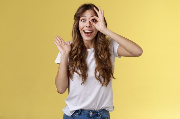 Oh hallo ich sehe dich. Fasziniertes süßes charmantes junges Mädchen, das mit der Palme winkt, sagt hallo beeindruckt durch die okay-Ring-Geste beeindruckt endlich fester Anblick stehen erstaunt erstaunt gelber Hintergrund