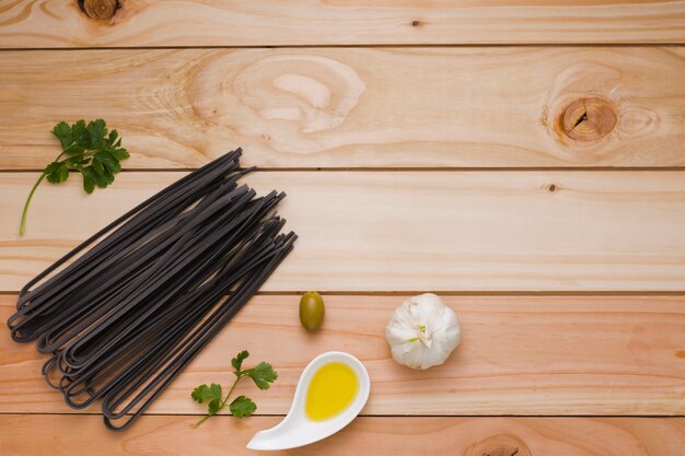 Olive; Knoblauch; Petersilie und ungekochte rohe schwarze Reisteigwaren auf Holztisch