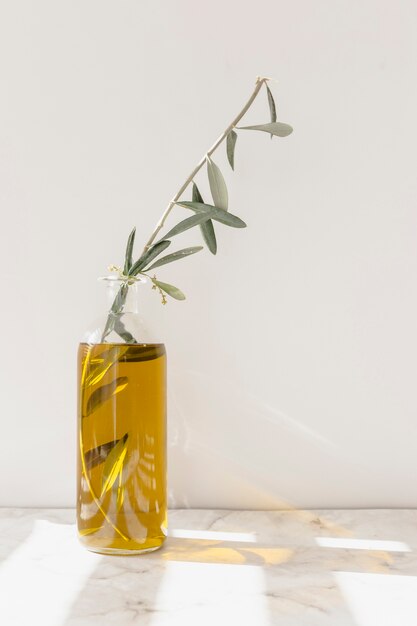 Olivenzweig innerhalb des gelben Öls in der Glasflasche auf dem Marmorboden