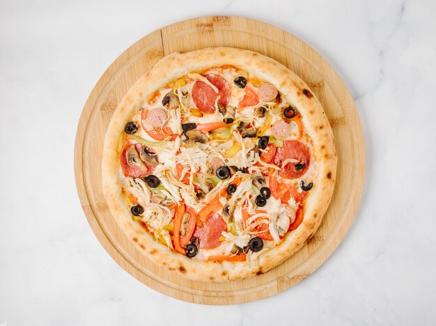 Olivgrüne Pizza der Pepperonis auf einer hölzernen Platte.