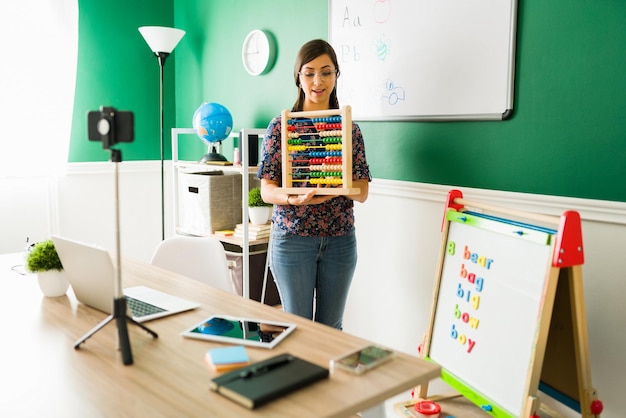 Online-Kindergarten-Konzept. Nette Vorschullehrerin mit Brille, die einen Abakus verwendet, um kleinen Kindern eine Matheklasse zu geben