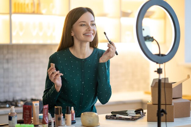 Online-Schönheitskurs. Junge Frau im grünen Kleid, die Make-up-Tipps online zeigt