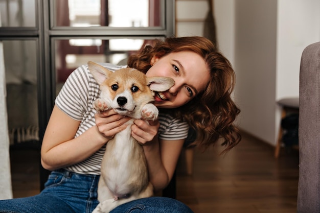 Optimistische Frau in Jeans sitzt auf dem Boden und spielt mit Hund Mädchen ist süß lächelnd