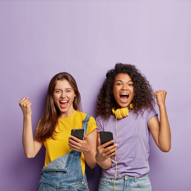 Optimistische Freundinnen posieren mit ihren Handys